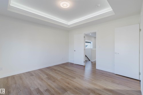 Tray ceiling with integrated lighting, recessed circular light fixture, wood-finish flooring, two white panel doors, and white walls - 6047 180 Avenue Nw, Edmonton, AB 