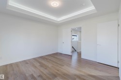 Tray ceiling with integrated lighting, recessed circular light fixture, wood-finish flooring, two white panel doors, and white walls - 