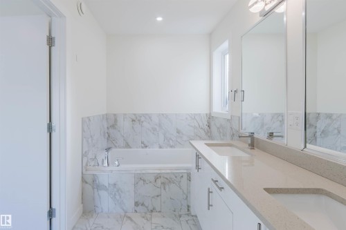 Dual vanity with integrated sinks, spacious countertop, undermount bathtub, and marble-look wall and floor tile - 6047 180 Avenue Nw, Edmonton, AB 