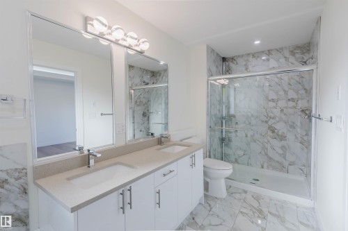 Dual vanity with integrated sinks and polished chrome faucets, large vanity mirrors, contemporary vanity lighting, glass-enclosed shower with tiled surround, and patterned floor tiling - 6047 180 Avenue Nw, Edmonton, AB 