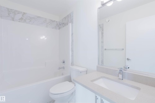 White bathtub/shower combination with chrome fixtures, marble-patterned tile accent, white toilet, vanity with integrated sink, and chrome faucet - 6047 180 Avenue Nw, Edmonton, AB 