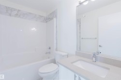 White bathtub/shower combination with chrome fixtures, marble-patterned tile accent, white toilet, vanity with integrated sink, and chrome faucet - 