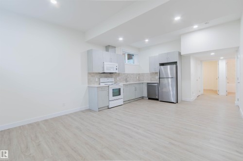 Kitchen with light gray cabinetry, stainless steel refrigerator and dishwasher, white range and microwave, and wood-finish flooring - 6047 180 Avenue Nw, Edmonton, AB 