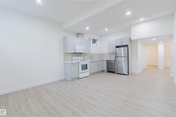 Kitchen with light gray cabinetry, stainless steel refrigerator and dishwasher, white range and microwave, and wood-finish flooring - 