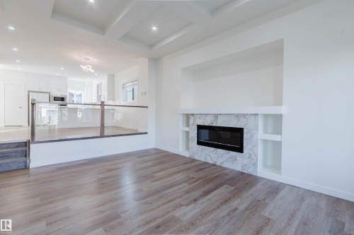 Hardwood-finish flooring throughout, tray ceiling with recessed lighting, and a modern fireplace with built-in shelving - 6047 180 Avenue Nw, Edmonton, AB 