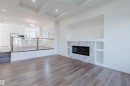 Hardwood-finish flooring throughout, tray ceiling with recessed lighting, and a modern fireplace with built-in shelving - 6047 180 Avenue Nw, Edmonton, AB 