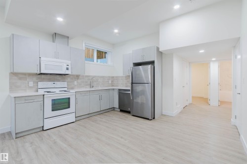 Modern kitchen with light grey cabinetry, white countertops, stainless steel appliances, and wood-finish flooring - 6047 180 Avenue Nw, Edmonton, AB 