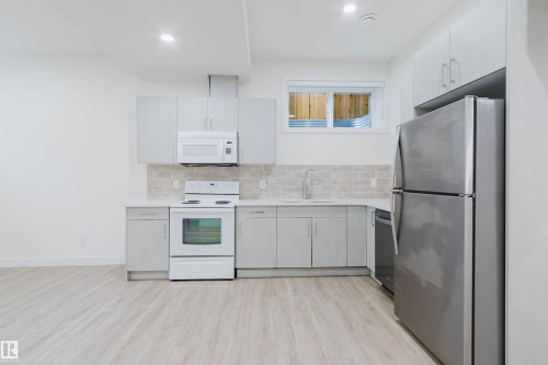 Kitchen featuring light wood-finish flooring, white cabinetry, light-toned countertops, tile backsplash, and stainless steel appliances - 6047 180 Avenue Nw, Edmonton, AB 