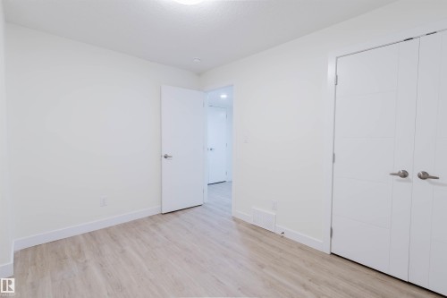 Light wood-finish flooring, white walls, modern ceiling light fixture, white interior door, and double closet doors with horizontal paneling - 6047 180 Avenue Nw, Edmonton, AB 