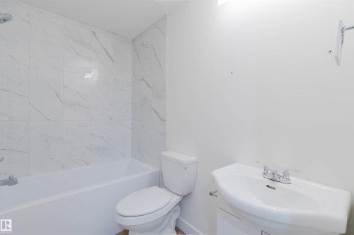 Bathtub with shower fixture, white subway tile surround, wall-mounted sink, and toilet - 6047 180 Avenue Nw, Edmonton, AB 