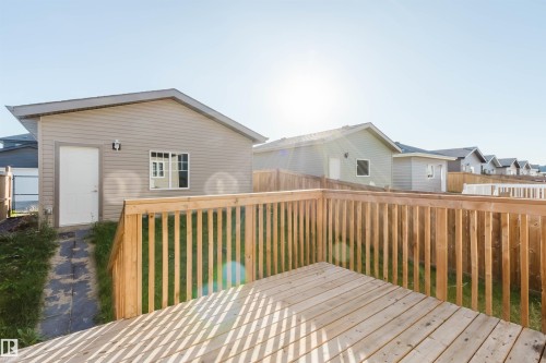 Spacious wood-finish deck with railing, detached auxiliary building with siding, pitched roof, and exterior lighting - 6047 180 Avenue Nw, Edmonton, AB 