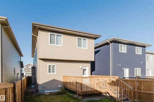 Rear exterior featuring a wood deck with stairs, beige horizontal siding, white-framed windows, and a wood fence - 6047 180 Avenue Nw, Edmonton, AB 