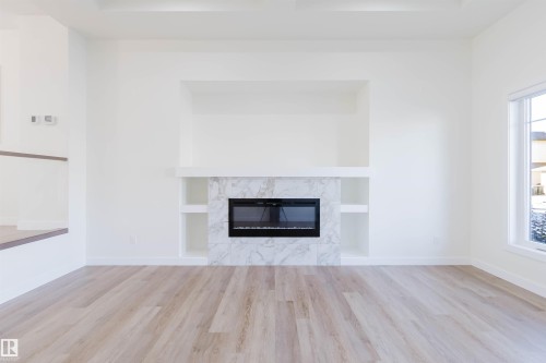 Wood-finish flooring, built-in electric fireplace with stone-finish surround, built-in shelving, wall niche, and large window - 6047 180 Avenue Nw, Edmonton, AB 