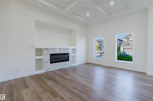 Tray ceiling with recessed lighting, wood-finish flooring, built-in electric fireplace with stone-finish surround, built-in shelving, and dual windows - 6047 180 Avenue Nw, Edmonton, AB 