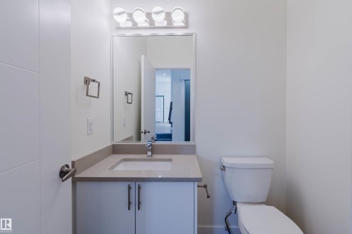 Modern bathroom featuring a single vanity with an undermount sink and light-toned countertop, a rectangular frameless mirror, and a four-bulb vanity light fixture - 6047 180 Avenue Nw, Edmonton, AB 