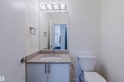 Modern bathroom featuring a single vanity with an undermount sink and light-toned countertop, a rectangular frameless mirror, and a four-bulb vanity light fixture - 