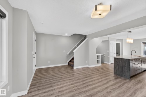 Open-concept design featuring wood-finish flooring, a kitchen island with built-in cabinetry, and a contemporary ceiling light fixture - #44 3025 151 Av Nw, Edmonton, AB 
