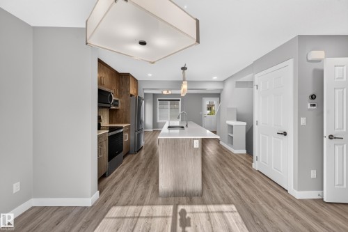 Open-concept kitchen with wood-finish flooring, light gray walls, and a center island featuring an undermount sink - #44 3025 151 Av Nw, Edmonton, AB 