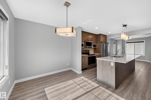 Modern kitchen featuring a large center island with a white countertop, stainless steel appliances, wood-finish cabinetry, and wood-finish flooring - #44 3025 151 Av Nw, Edmonton, AB 