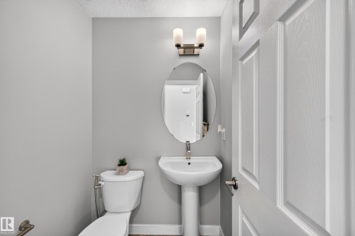 Powder room featuring a pedestal sink with chrome fixtures, an oval framed mirror, and dual sconce lighting above - #44 3025 151 Av Nw, Edmonton, AB 