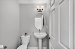Powder room featuring a pedestal sink with chrome fixtures, an oval framed mirror, and dual sconce lighting above - 