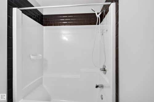 White fiberglass tub and shower combination with dark subway tile surround, featuring a chrome shower head and bath spout - #44 3025 151 Av Nw, Edmonton, AB 