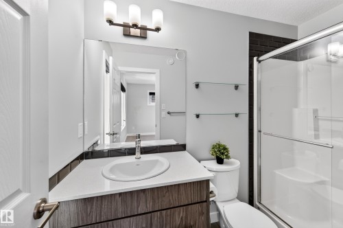 Vanity with a white countertop and wood-finish cabinetry, under-mount sink with a chrome faucet, and a large wall-mounted mirror - #44 3025 151 Av Nw, Edmonton, AB 