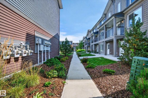Multi-level structures with balconies, dark siding, and manicured landscaping, featuring a concrete pathway - #44 3025 151 Av Nw, Edmonton, AB 