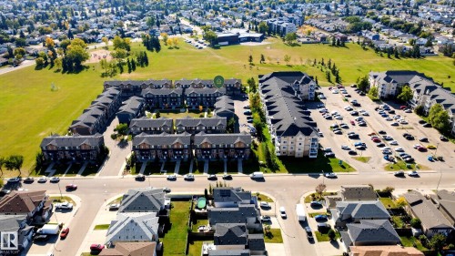Aerial perspective showcasing a residential area with townhomes and multi-story buildings, featuring multiple parking areas and surrounding green spaces - #44 3025 151 Av Nw, Edmonton, AB 
