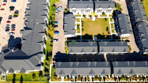 Community featuring multiple residential structures with dark shingle roofs, paved roadways, and integrated green spaces - #44 3025 151 Av Nw, Edmonton, AB 