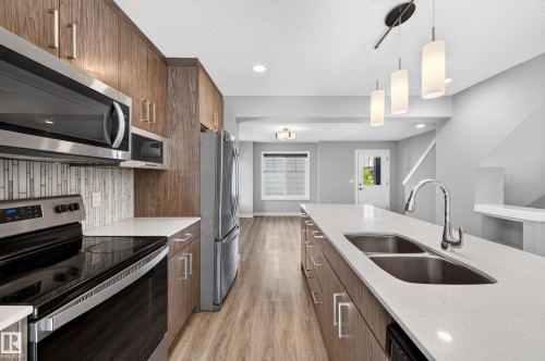 Kitchen featuring wood-finish cabinetry, stainless steel appliances, white countertops, and an undermount double-basin sink - #44 3025 151 Av Nw, Edmonton, AB 