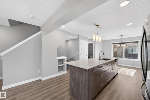 Modern kitchen island with a light-toned countertop, integrated sink, and dishwasher - #44 3025 151 Av Nw, Edmonton, AB 