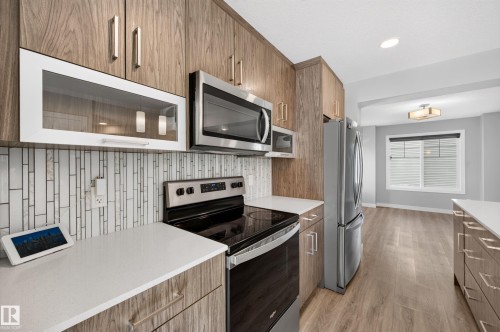 Kitchen featuring wood-finish cabinetry, stainless steel appliances, white countertops, and a full-height tile backsplash - #44 3025 151 Av Nw, Edmonton, AB 