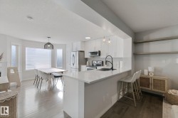 Open-concept living space with light wood-finish flooring, white cabinetry, integrated stainless steel appliances, and a kitchen island with seating - 