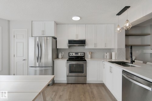 White cabinetry with brushed nickel hardware, stainless steel appliances, light wood-finish flooring, white countertops, and a herringbone tile backsplash - 8535 Ellis Link Link Nw, Edmonton, AB 