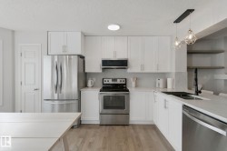 White cabinetry with brushed nickel hardware, stainless steel appliances, light wood-finish flooring, white countertops, and a herringbone tile backsplash - 
