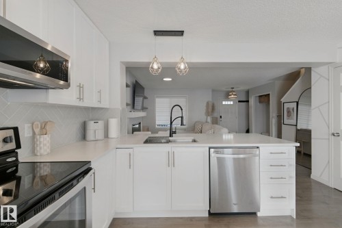 White cabinetry, stainless steel appliances, herringbone tile backsplash, white countertops, and contemporary pendant lighting - 8535 Ellis Link Link Nw, Edmonton, AB 
