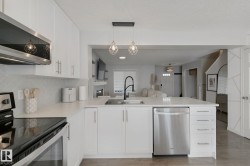 White cabinetry, stainless steel appliances, herringbone tile backsplash, white countertops, and contemporary pendant lighting - 
