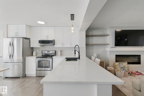 Modern kitchen featuring stainless steel appliances, white cabinetry, a large island with a black gooseneck faucet, and wood-finish flooring - 8535 Ellis Link Link Nw, Edmonton, AB 