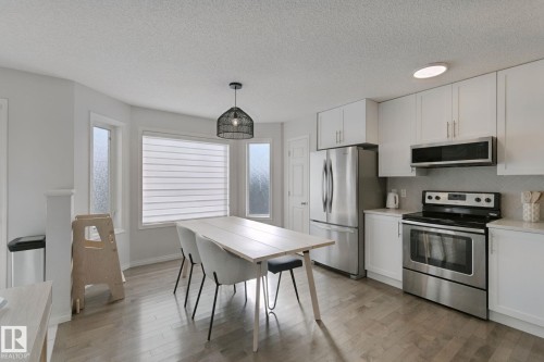 Kitchen featuring stainless steel appliances, white cabinetry, light wood-finish flooring, and a dining area with a modern pendant light fixture - 8535 Ellis Link Link Nw, Edmonton, AB 