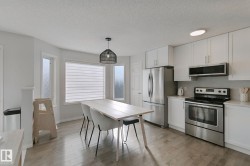 Kitchen featuring stainless steel appliances, white cabinetry, light wood-finish flooring, and a dining area with a modern pendant light fixture - 
