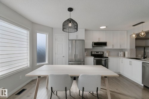 Light wood-finish flooring, white cabinetry, stainless steel appliances, and a textured tile backsplash - 8535 Ellis Link Link Nw, Edmonton, AB 