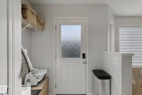 White paneled door with privacy glass, adjacent window with horizontal blinds, built-in half-wall partition, and wire shelving system - 8535 Ellis Link Link Nw, Edmonton, AB 