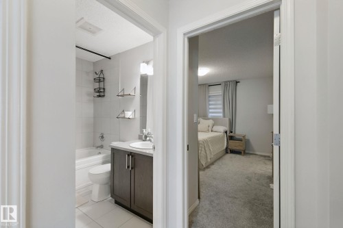 Bathroom with a bathtub, white tile surround, and a dark wood-finish vanity with an integrated sink - 8535 Ellis Link Link Nw, Edmonton, AB 
