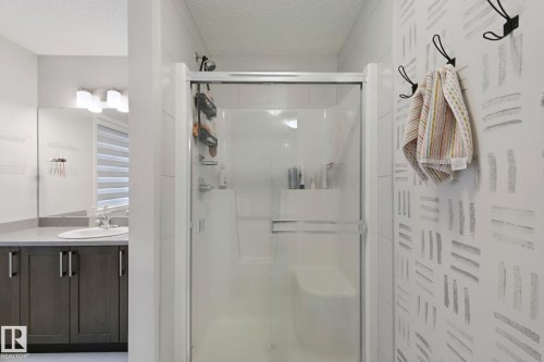 Glass-enclosed shower with integrated seating, a vanity with a rectangular sink, dark wood-finish cabinetry, light stone-finish countertop, and a vanity mirror - 8535 Ellis Link Link Nw, Edmonton, AB 