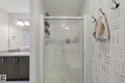 Glass-enclosed shower with integrated seating, a vanity with a rectangular sink, dark wood-finish cabinetry, light stone-finish countertop, and a vanity mirror - 