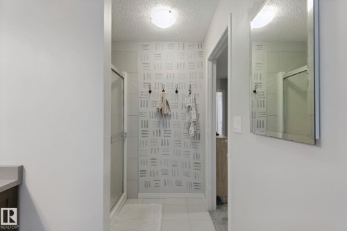 Glass-enclosed shower with a sliding door, tile flooring, and a flush-mount ceiling light fixture - 8535 Ellis Link Link Nw, Edmonton, AB 
