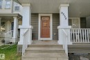 Covered porch entrance with wood stairs, white railing, and a wood-panel door - 8535 Ellis Link Link Nw, Edmonton, AB 