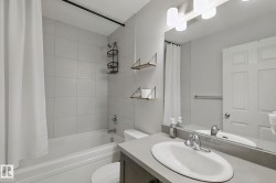 White subway-tiled shower surround with a built-in tub, a single-sink vanity with a light gray countertop, and a vanity mirror with overhead lighting - 