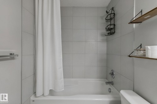 Bathtub with tiled surround, chrome fixtures, and wall-mounted shelving - 8535 Ellis Link Link Nw, Edmonton, AB 
